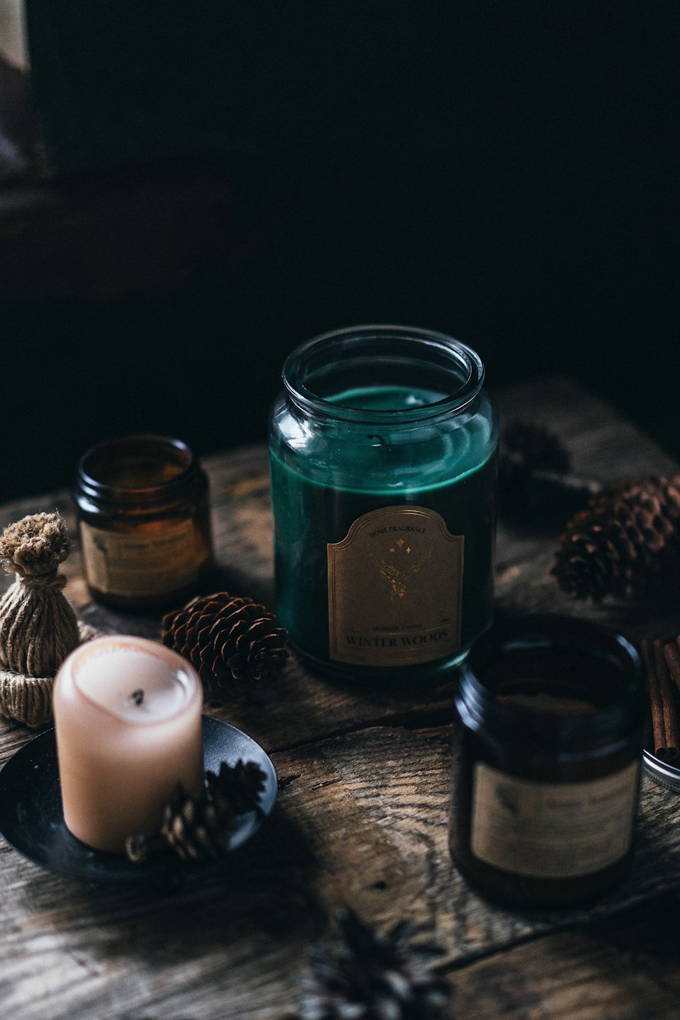 Green and beige candles sit on a wooden table with pinecones.